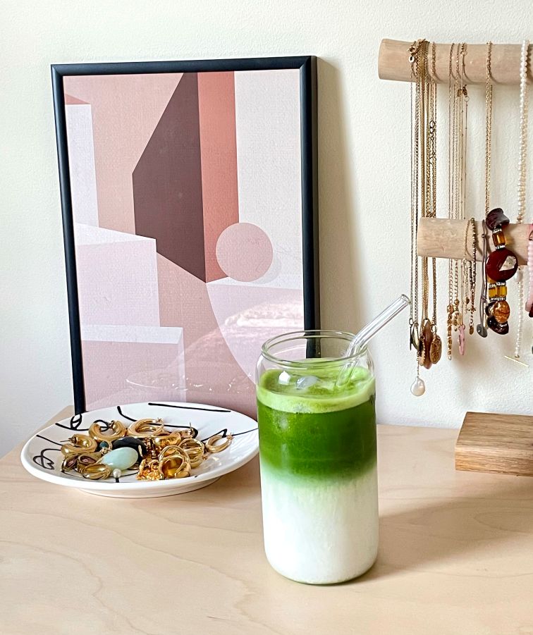 Iced matcha latte in a tall glass with a straw and ice cubes. On a piece of furniture with jewels.