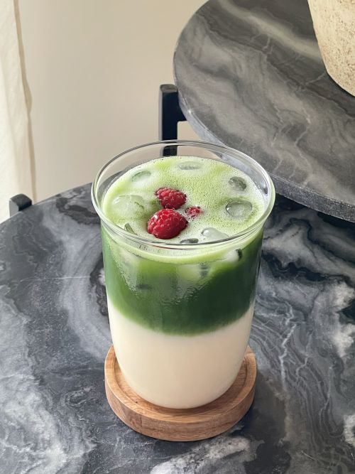 Iced matcha latte in a large clear glass, with raspberries on top. Set on a marble table.