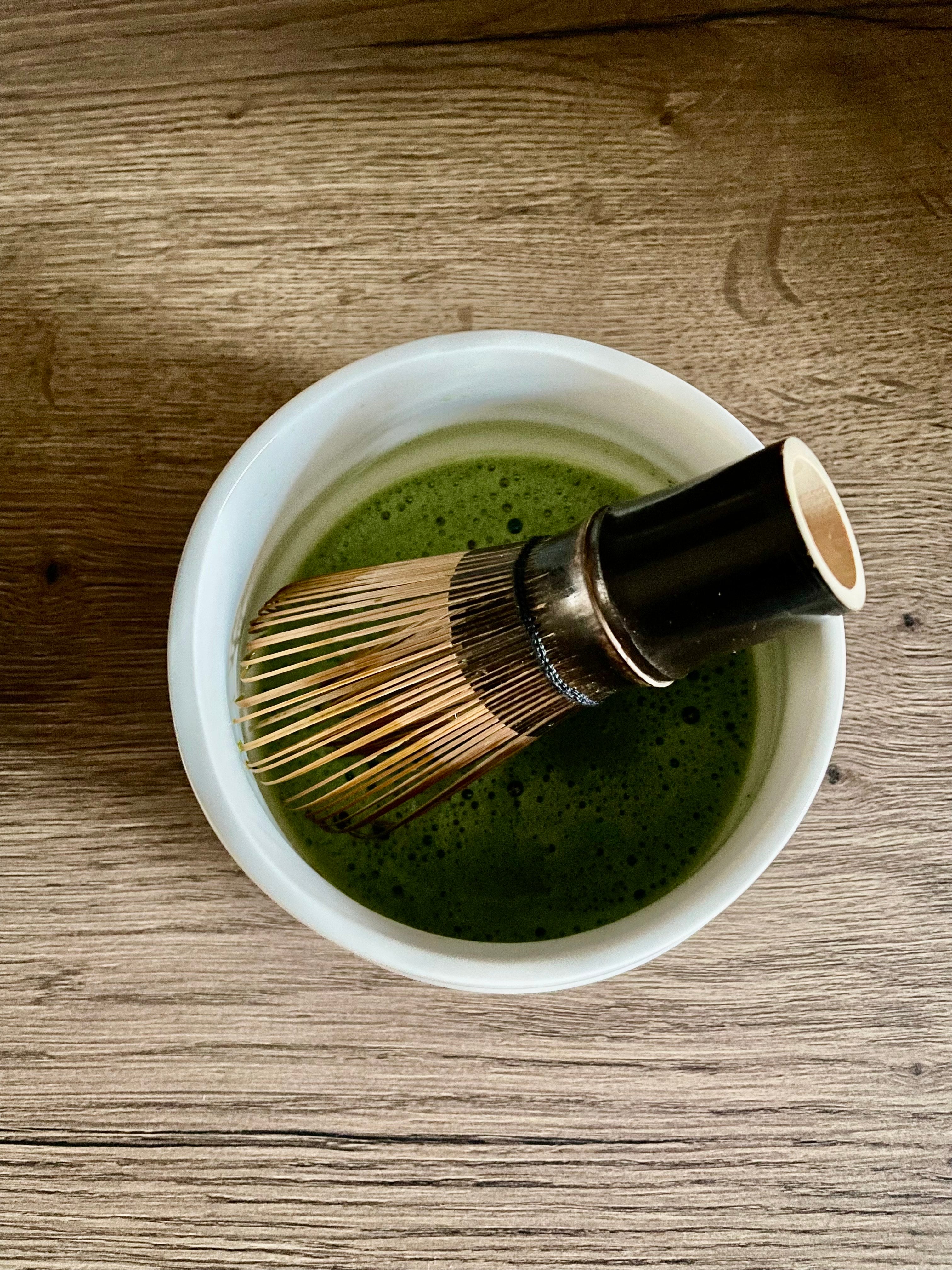 Bamboo whisk in a matcha bowl filled with foamy matcha tea
