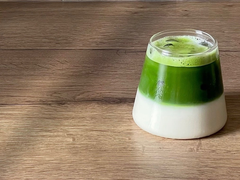 Banner showing an iced matcha latte in a wide glass, with a narrower top. Ice cubes visible on top.