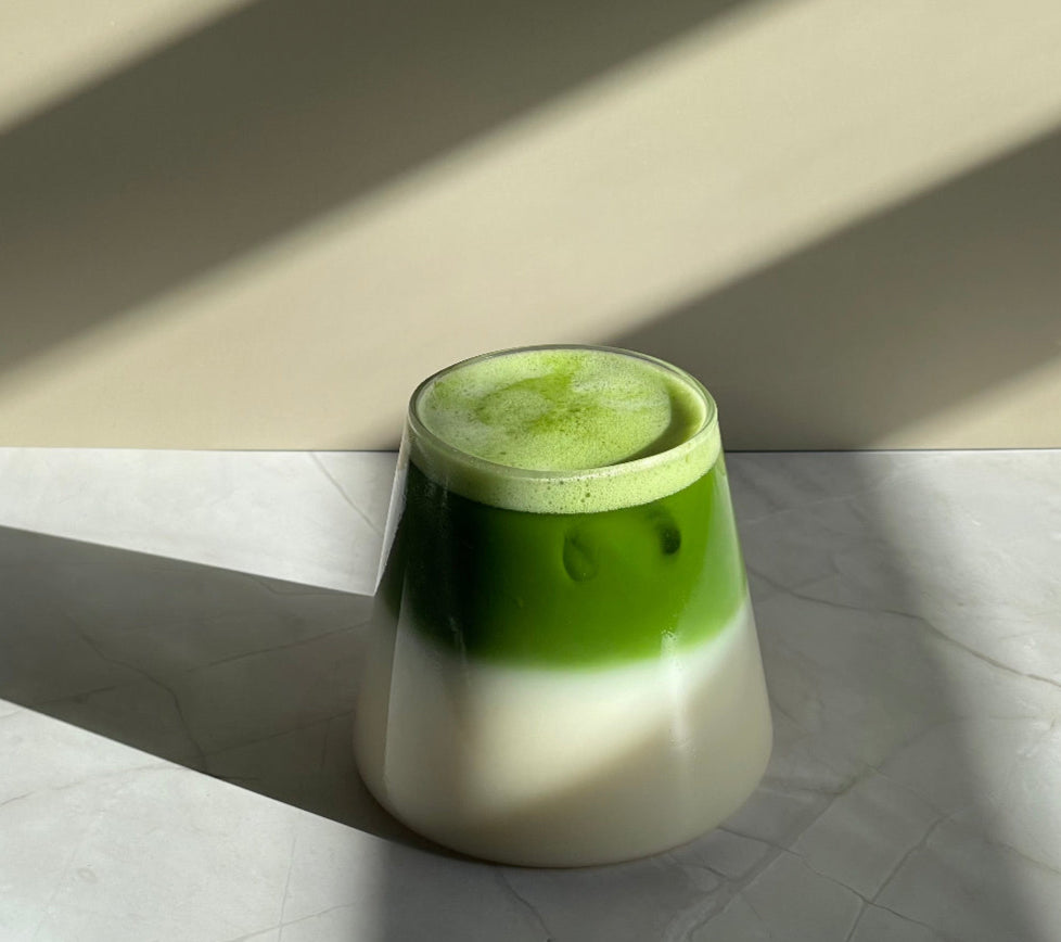 Sparkling Matcha latte in a clear conical glass, on a marble base, with shadow play at the front.