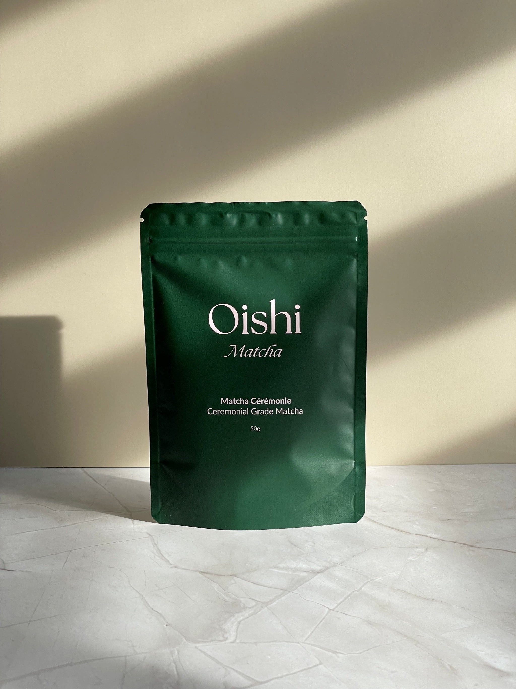 Oishi Matcha tea bag, front, on marble base with beige background.