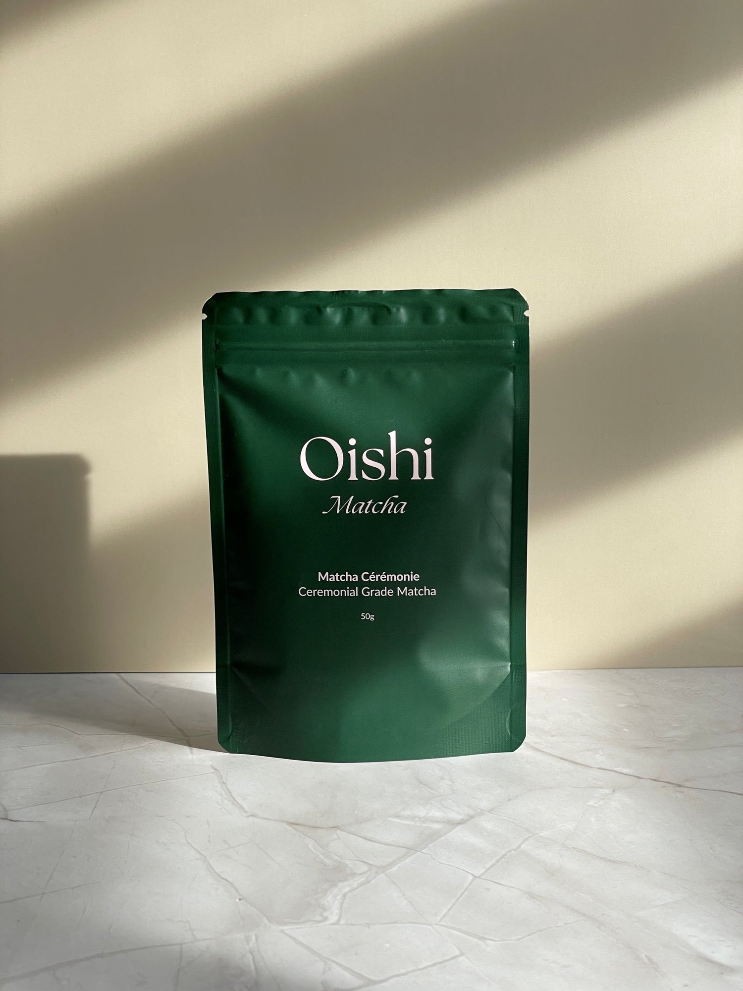 Oishi Matcha tea bag, front, on marble base with beige background.