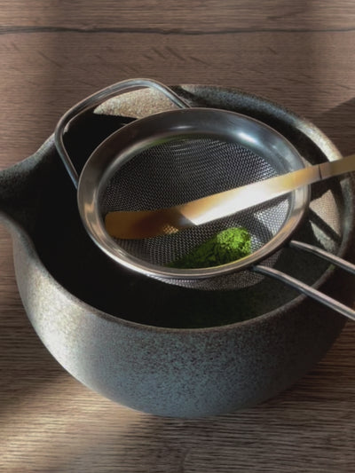 Poudre de matcha tamisée à travers sur une passoire dans un bol
