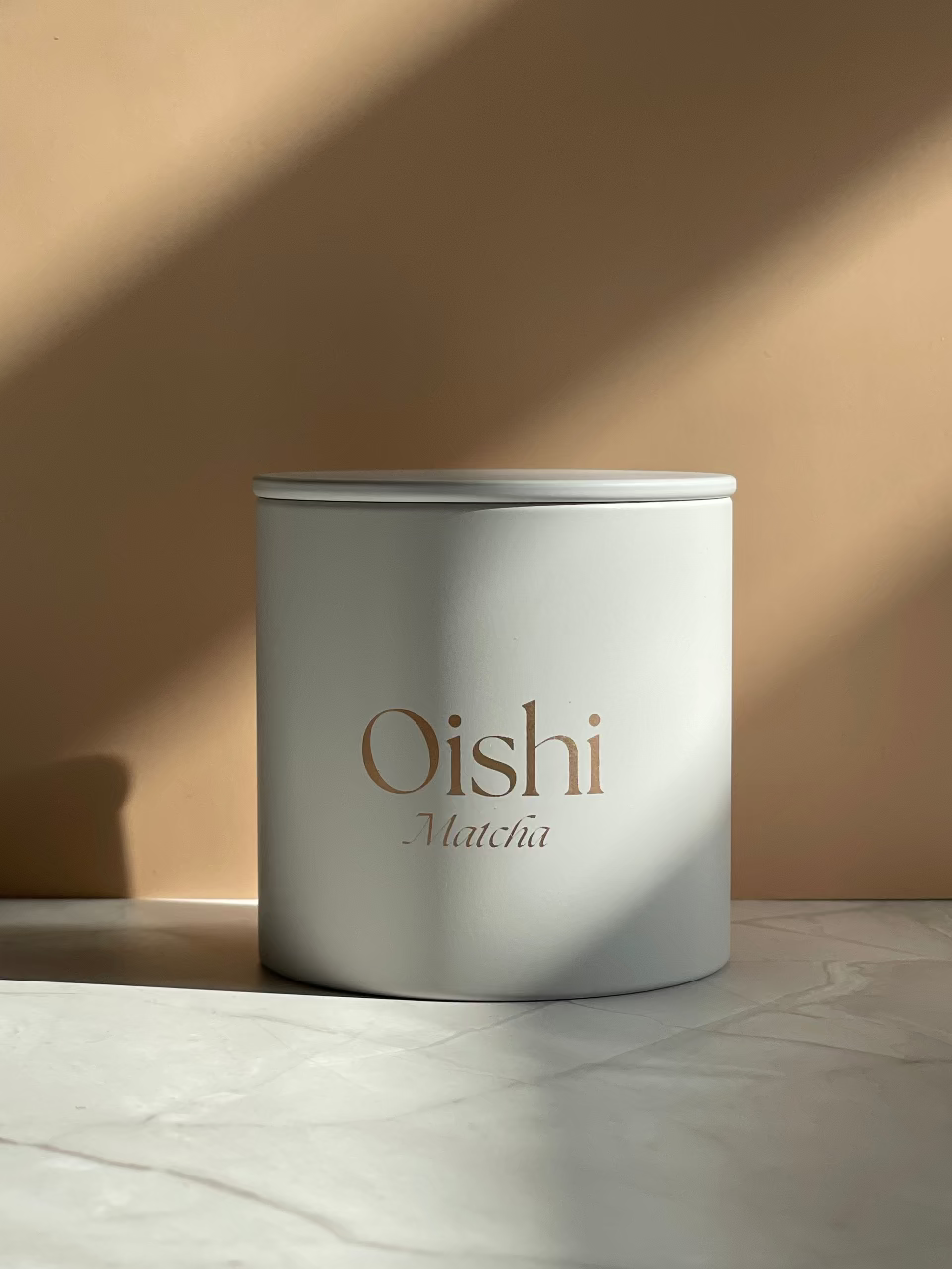 Weiße zylindrische Teedosen mit dem goldenen Oishi Matcha Logo.