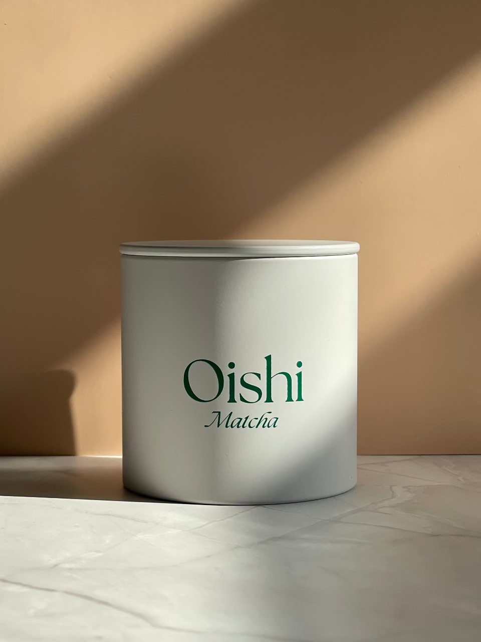 Weiße zylindrische Teedosen mit dem goldenen Oishi Matcha Logo.